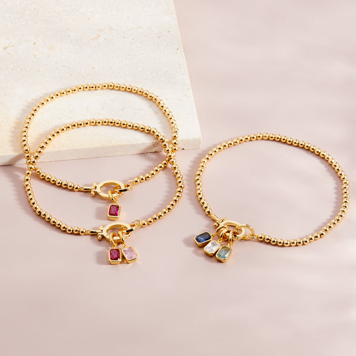 Two gold bracelets with colorful charms on a light background