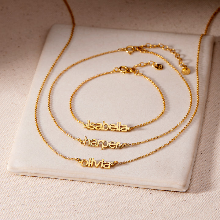 Three gold name bracelets on a white cushion