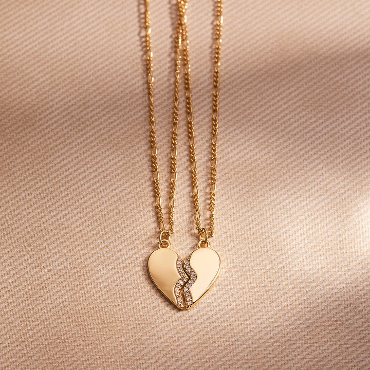 Gold heart-shaped pendant necklace on a beige fabric background