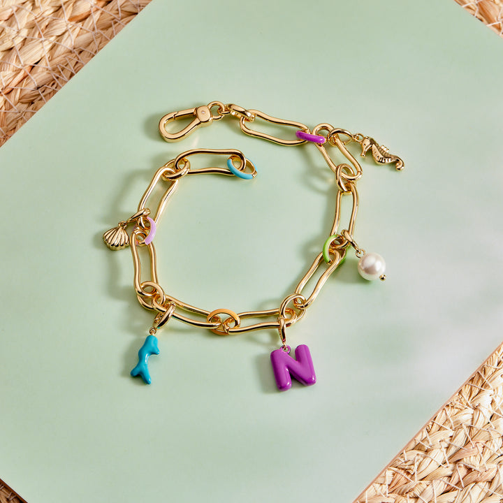 Gold chain bracelet with various charms on a green surface