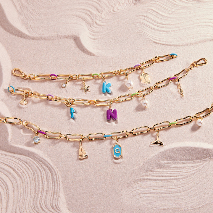 Gold chain bracelet with colorful charms on a textured beige background