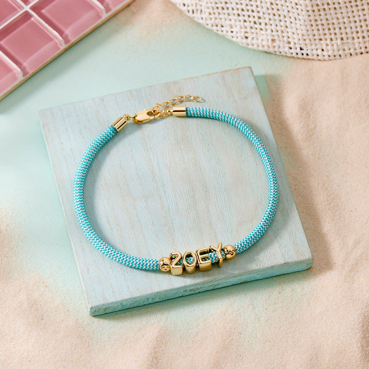 Blue braided bracelet with gold charm on a light stone surface