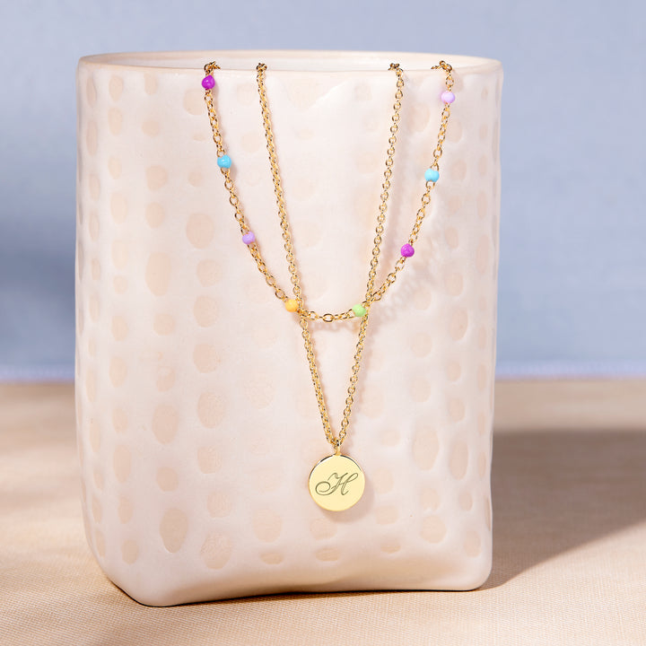 Two gold necklaces with colorful beads on a textured white surface