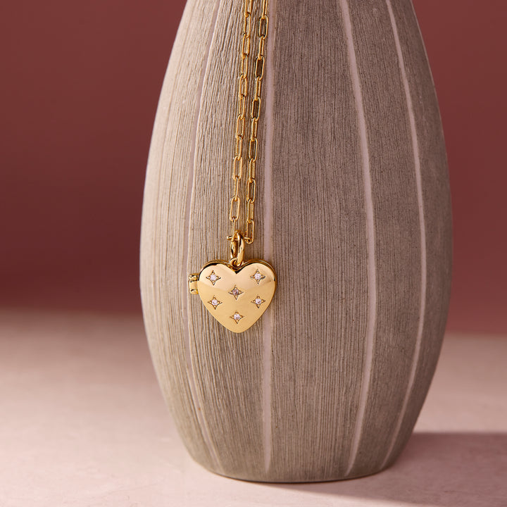  Heart locket necklace with five star-set crystal accents on a polished domed pendant, draped on a textured ceramic vase.