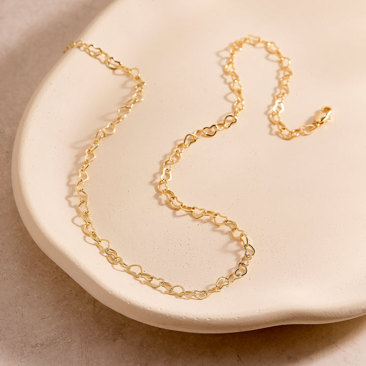  Seraphina Heart Necklace with open heart-shaped links and a lobster clasp, draped across a ceramic tray.