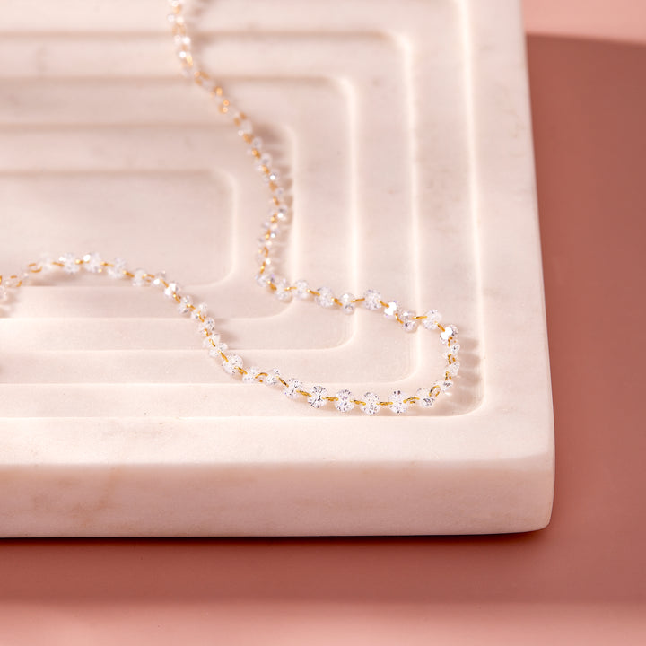  Chanel Floating Tennis Necklace draped on a marble tray, with round crystal stations linked along the full length.