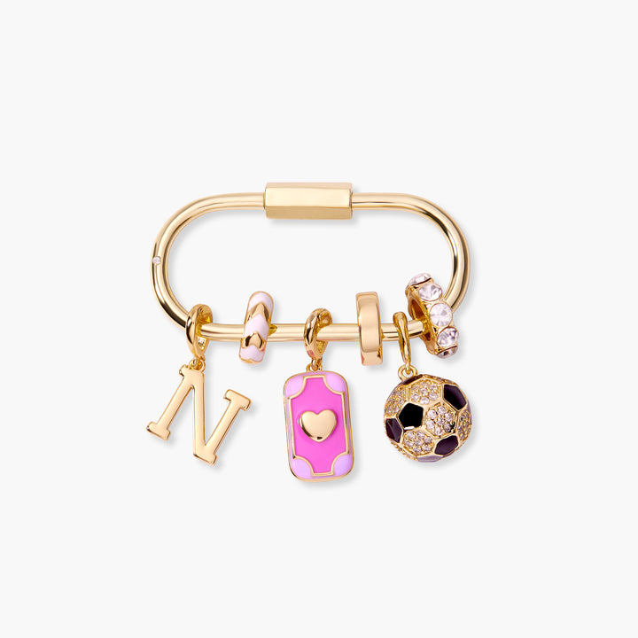 Charm key chain with a carabiner-style clasp holding an initial letter, pink enamel rectangular heart charm, crystal flower bead, and pavé soccer ball charm.