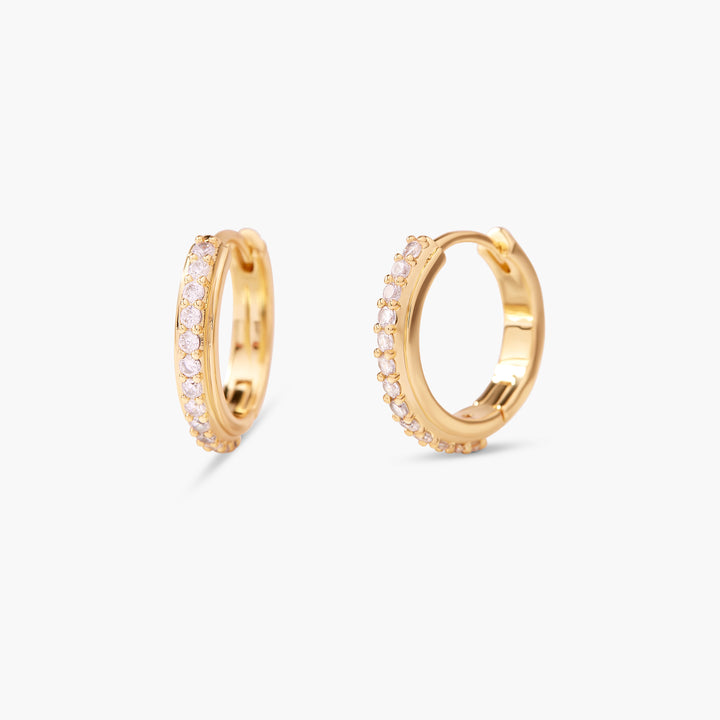 Small gold-tone huggie hoop earrings with a row of pavé-set round crystals along the outer face.