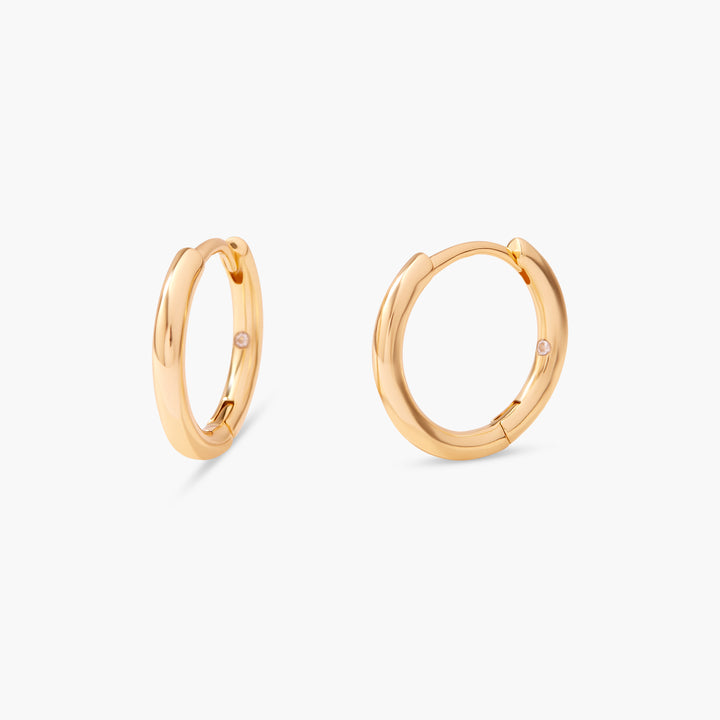 Pair of gold-tone Vivienne Huggie hoop earrings with a polished finish and a small flush-set stone on each hoop.