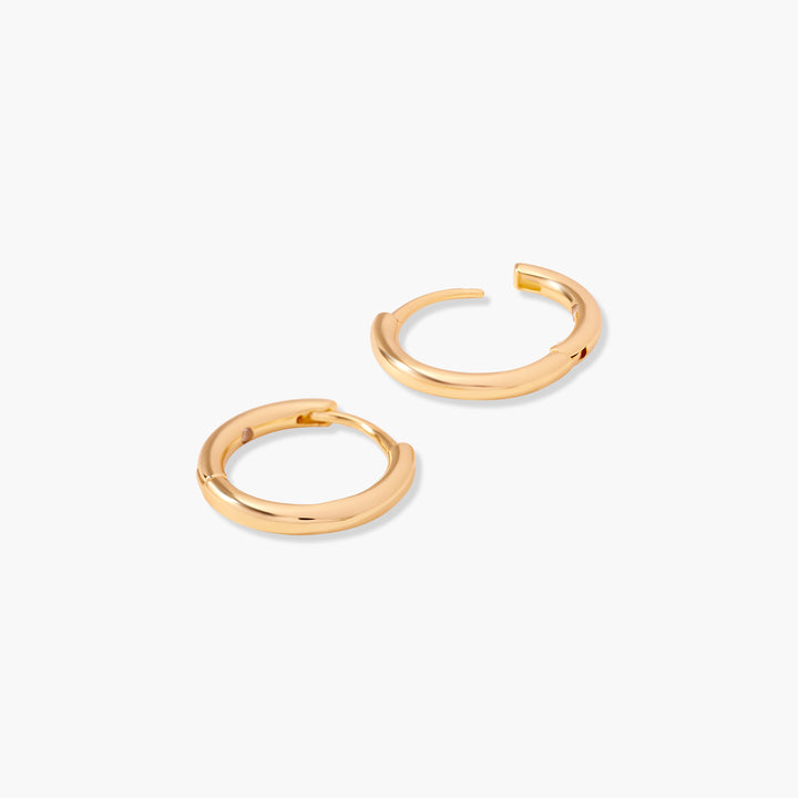  Pair of smooth polished huggie hoop earrings with a hinged closure, shown from an angled overhead view.