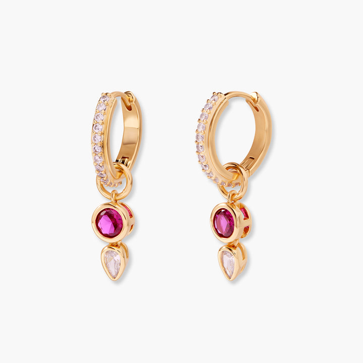 Gold-tone pavé huggie earrings with a dangling bezel-set round ruby stone above a teardrop crystal charm.