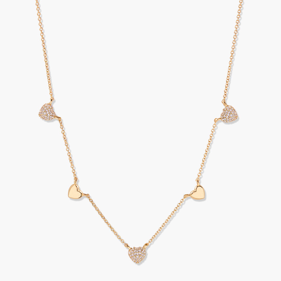 Gold-tone station necklace with five alternating pavé crystal and polished heart charms spaced along a delicate chain.