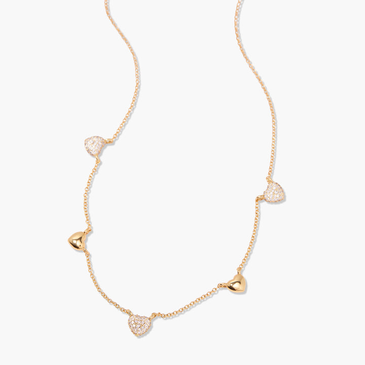 Station necklace with five alternating pavé crystal and polished heart charms spaced along a delicate chain, angled flat-lay view.