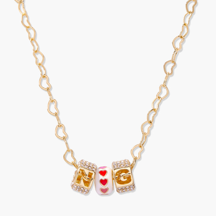 Charm necklace with two crystal-edged initial letter beads and a heart-motif enamel bead on a heart-link chain.