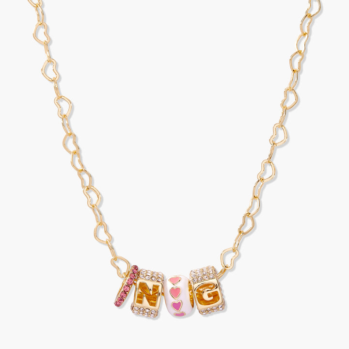 Customizable charm necklace with two block-letter initial charms, a pave-set spacer bead, and a pink enamel heart bead on a heart-link chain.