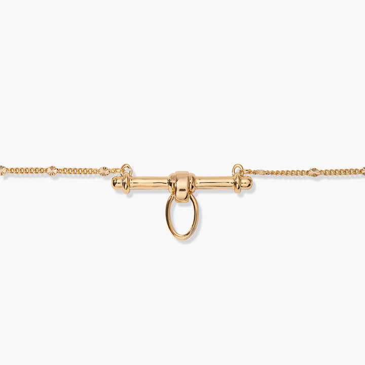  Close-up of the Poppy Bar Charm Necklace pendant, a polished horizontal bar with a central knot and oval ring clasp on a studded chain.