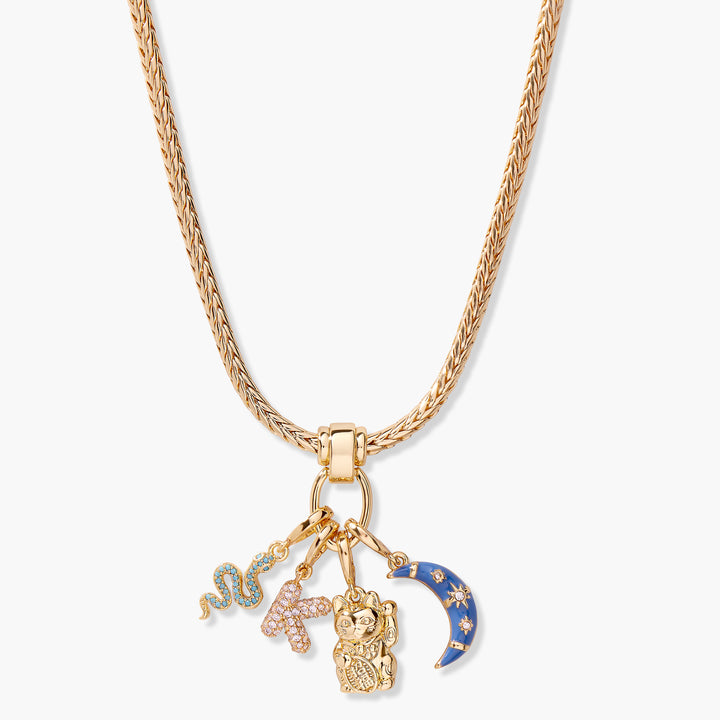 Charm necklace with a ring clasp holding a pavé snake, cross, lucky cat, and blue enamel crescent moon charm on a woven chain.