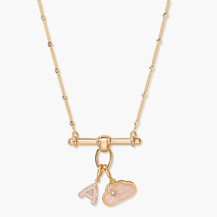 Charm necklace with a toggle bar pendant, a pavé block-letter initial charm, and a pink opal cloud charm with a star detail.