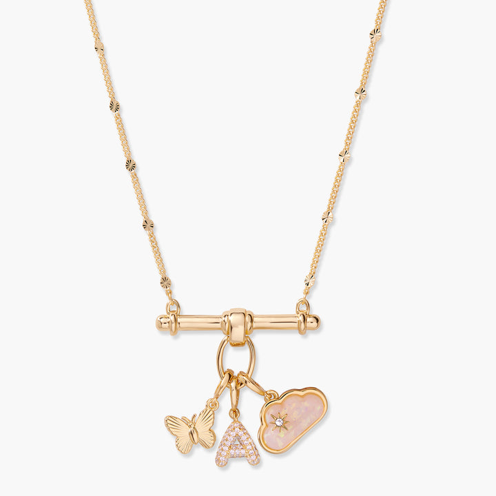 Charm necklace with a T-bar pendant holding a butterfly charm, a pavé initial letter charm, and an opal cloud charm with a star accent.
