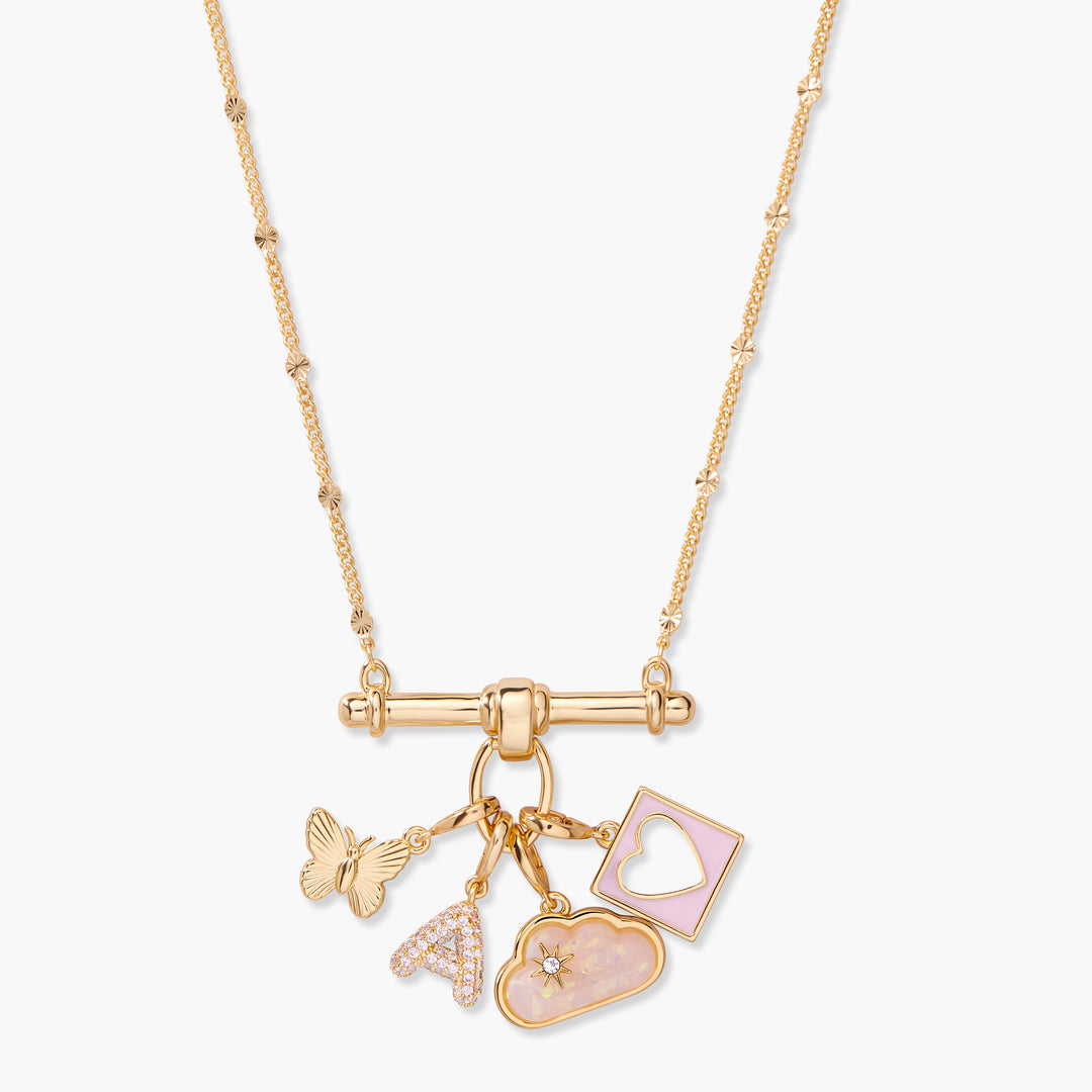 Gold-tone charm bar necklace with four dangling charms: a butterfly, a pavé initial letter, a pink opal cloud, and a rectangular pink enamel heart cutout pendant.