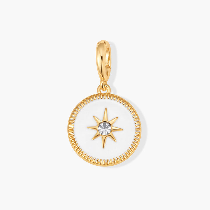 Gold-tone round Poppy North Star Charm with white enamel, a starburst center set with a clear crystal, and a milgrain border on a ring clasp.