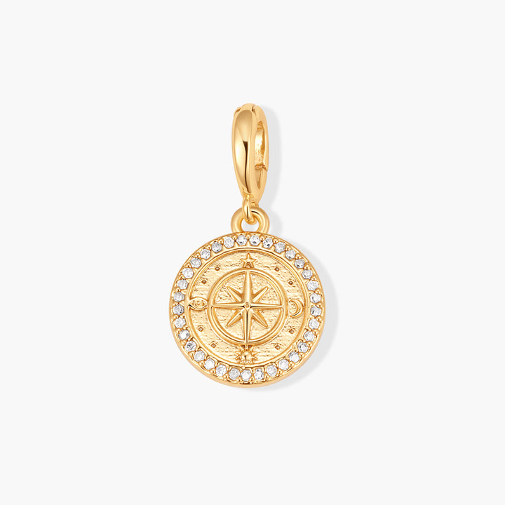 Gold-tone round compass charm with an engraved celestial compass rose and a pavé crystal border, attached to a ring clasp.