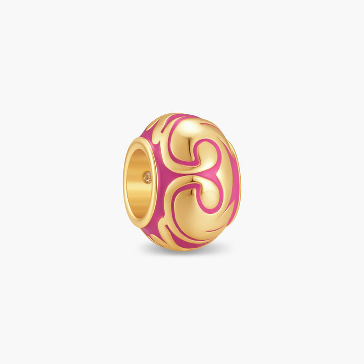 Round gold-tone Gaby Baroque Bead charm with bold swirling raised relief pattern filled with vibrant pink enamel.