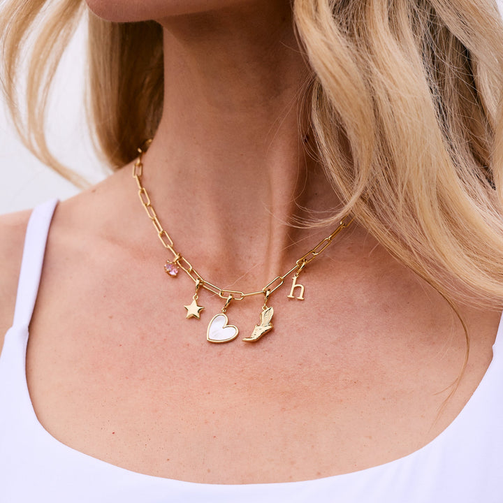 A close-up lifestyle shot of a woman wearing a delicate gold necklace with small celestial charms (star, crescent moon, and sun) and a matching gold bracelet on her wrist, paired with a white tank top.