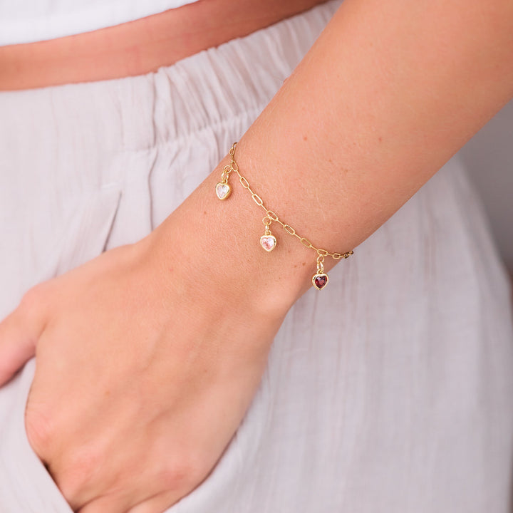  Mackenzie Heart Birthstone charm bracelet with three bezel-set heart-shaped stones in mixed colors, worn by a model.