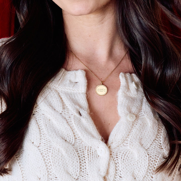 Cece Coordinate Necklace with a round pavé-bordered disc pendant engraved with custom coordinates, on a chain on a models neck.