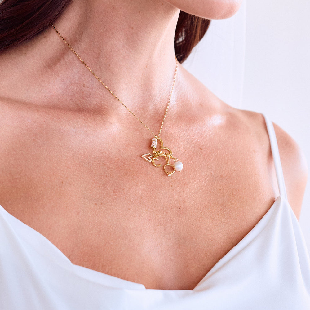  Mrs. Carabiner Charm Necklace resting on a models chest with a heart carabiner clasp, pavé heart, letter initial, ring, and pearl charms.
