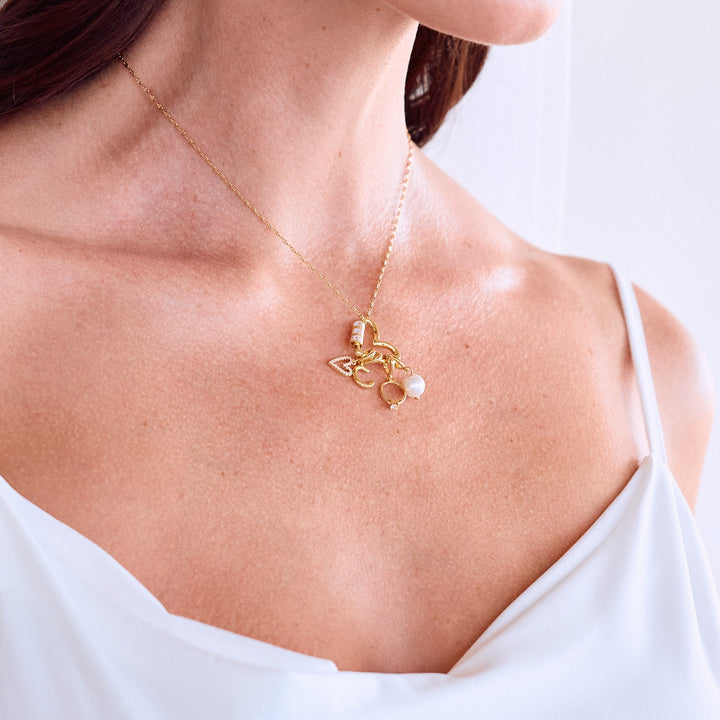  Mrs. Carabiner Charm Necklace resting on a models chest with a heart carabiner clasp, pavé heart, letter initial, ring, and pearl charms.