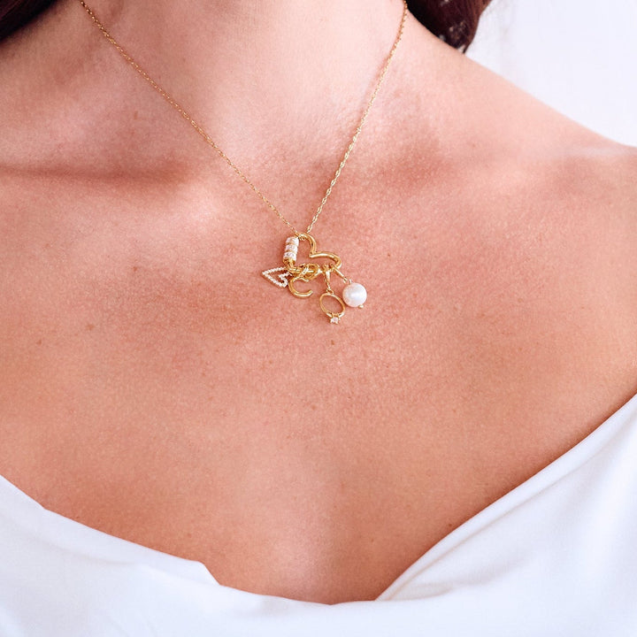 Mrs. Carabiner Charm Necklace resting on a models chest with a heart carabiner clasp, pavé heart, letter initial, ring, and pearl charms.