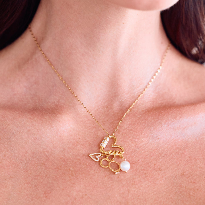 Mrs. Carabiner Charm Necklace resting on a models chest with a heart carabiner clasp, pavé heart, letter initial, ring, and pearl charms.