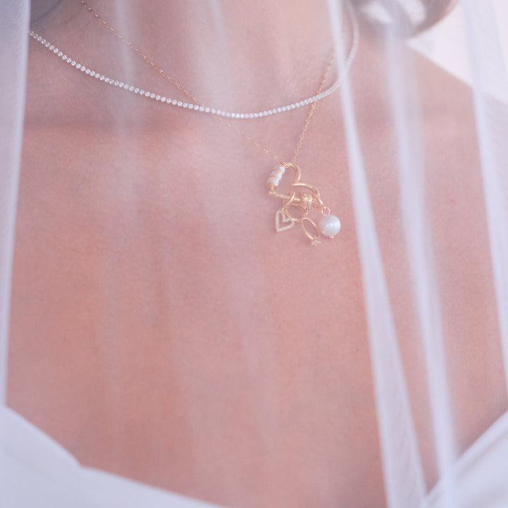 Mrs. Carabiner Charm Necklace resting on a models chest with a heart carabiner clasp, pavé heart, letter initial, ring, and pearl charms.