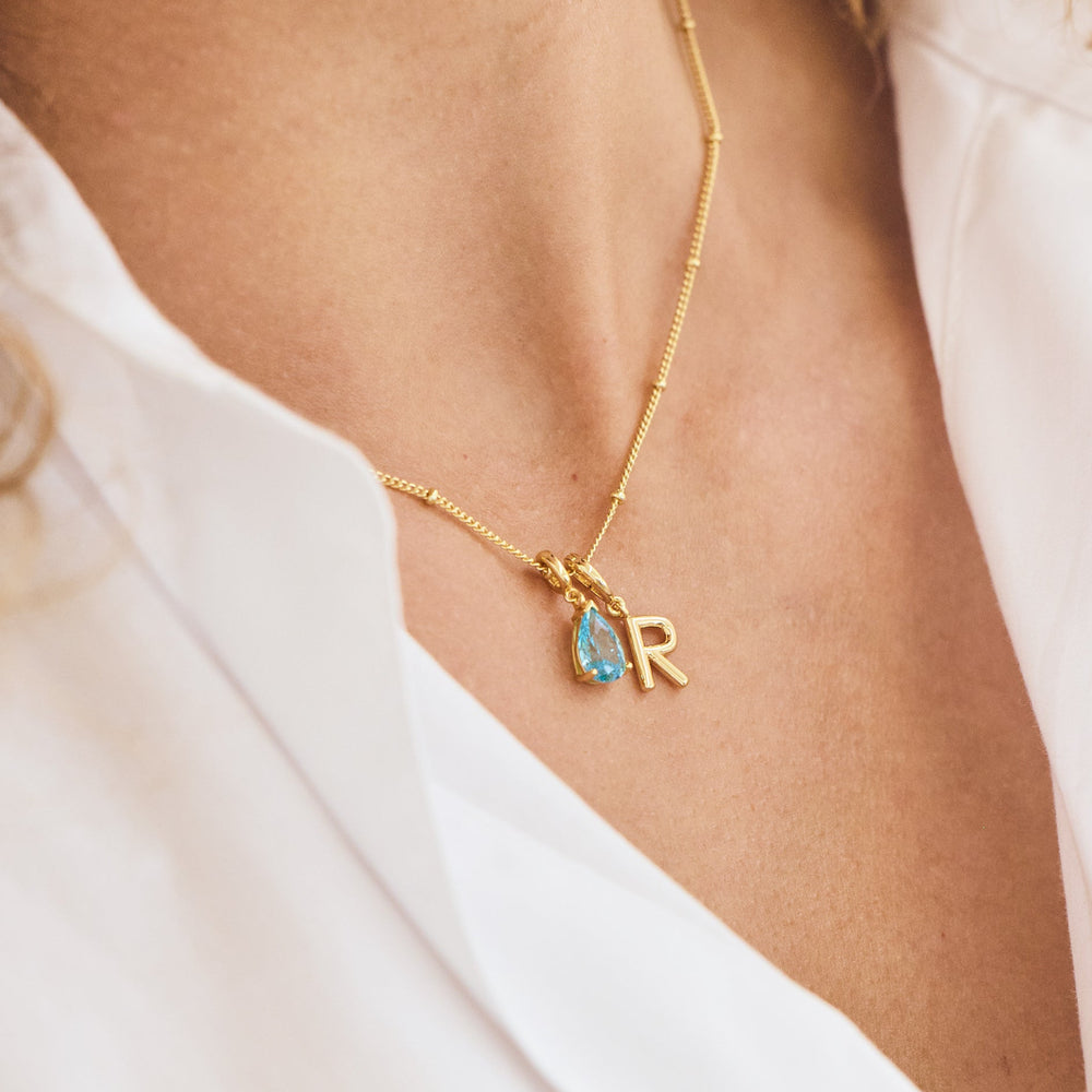  Melrose Birthstone Initial Necklace with a pear-cut blue birthstone charm and an initial letter charm, worn by a model.