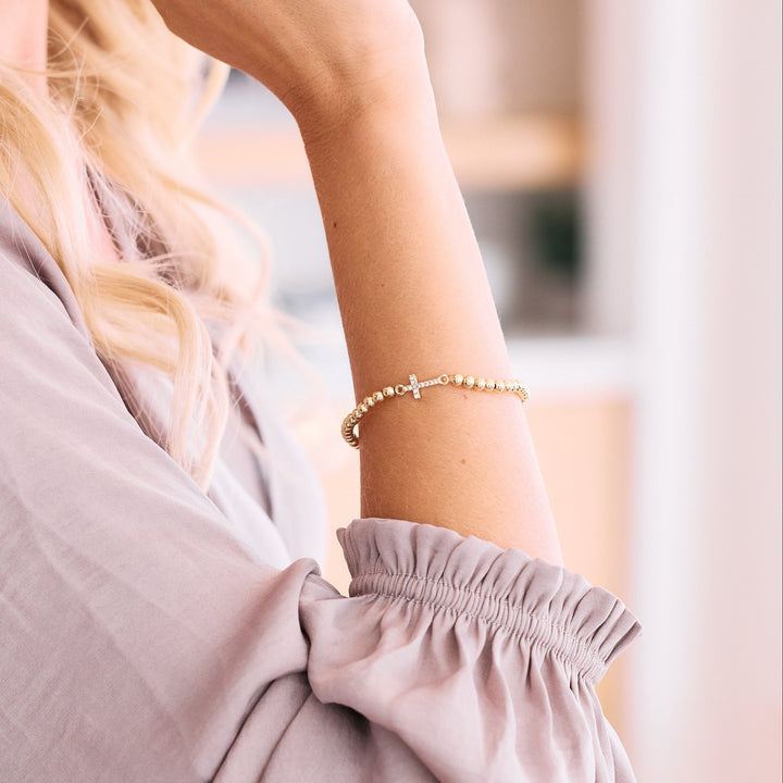 gold beaded bracelet with cz cross on arm.