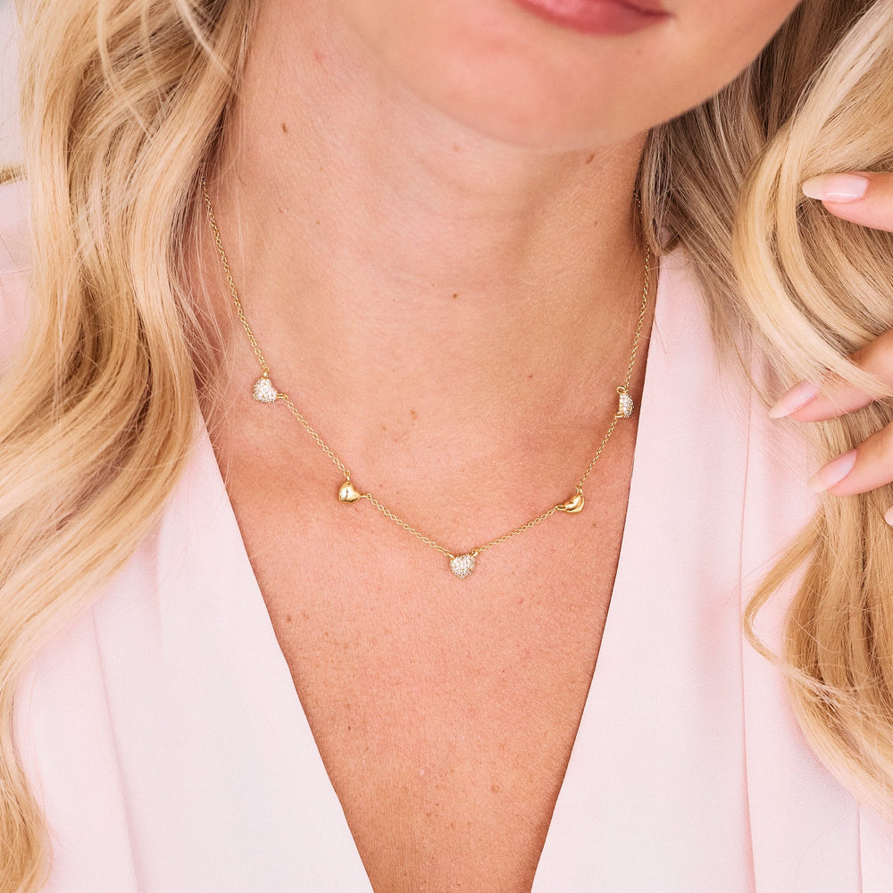  Posy Crystal Heart Necklace with five alternating pavé and polished heart charms on a chain, worn by a model.
