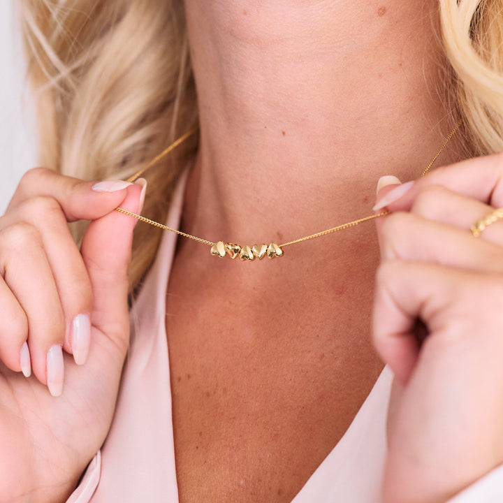 Posy Heart Necklace with five puffy heart charms on a delicate chain, worn by a model.