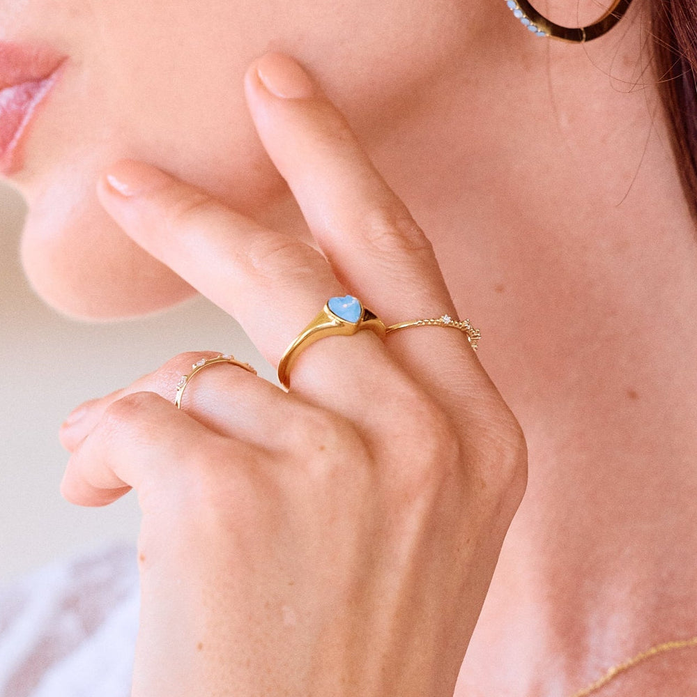  Heart signet ring with a blue opal heart stone on models hand.
