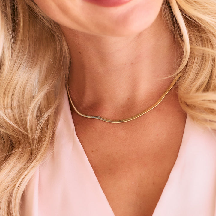 gold herringbone chain necklace on women wearing pink shirt.
