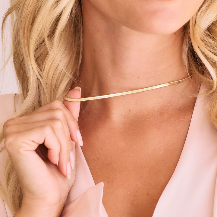 gold herringbone chain necklace on women wearing pink shirt.