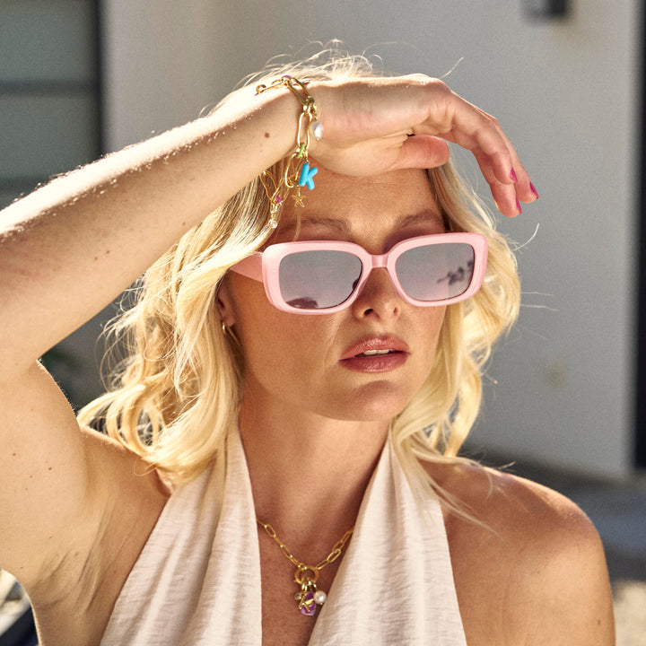 Woman wearing pink sunglasses and a white towel, standing outdoors.